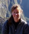 A woman in grey jacket standing on top of a mountain.